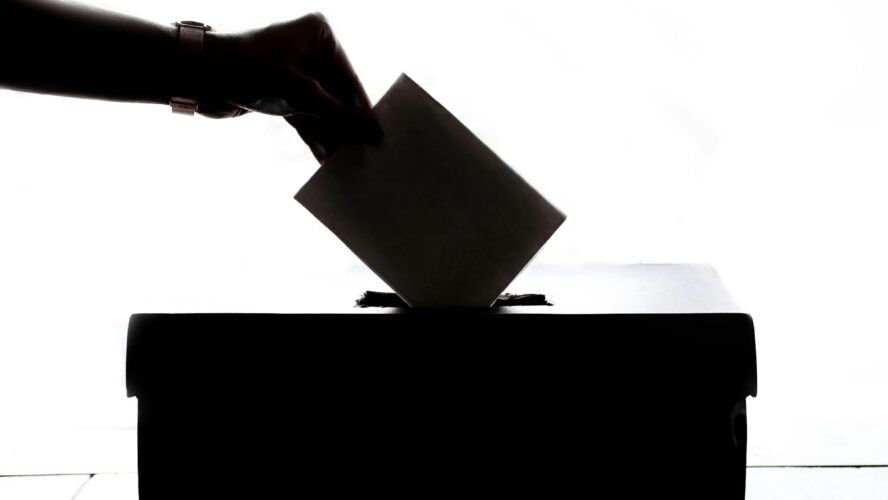 Silhouette of a hand holding a ballot paper about to drop it into a ballot box