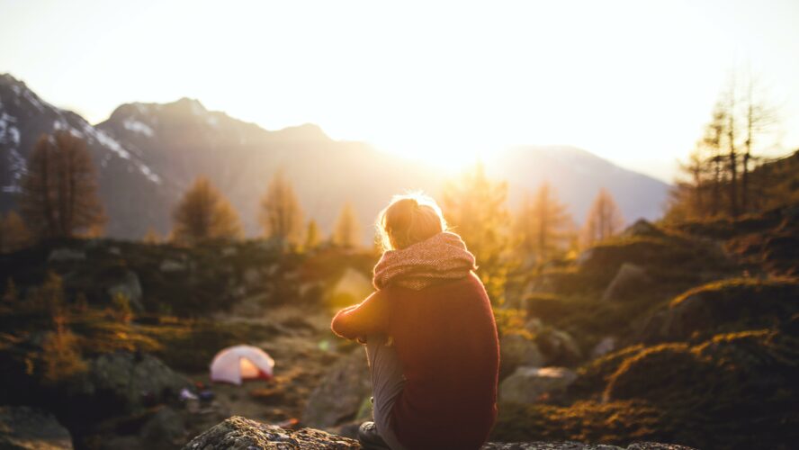 A person sitting with their back to the camera looking at a beautiful view of some mountains at sunset.