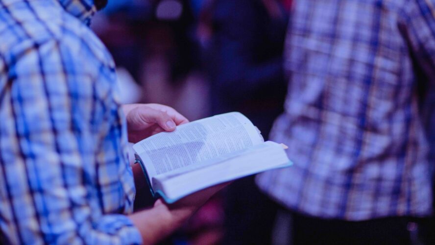 Older male stood holding a bible open.