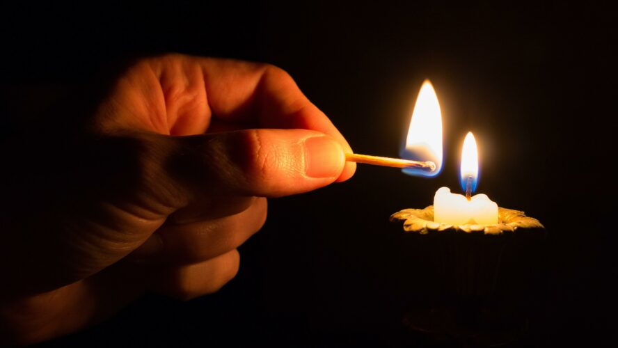 Hand holding a match, lighting a candle.
