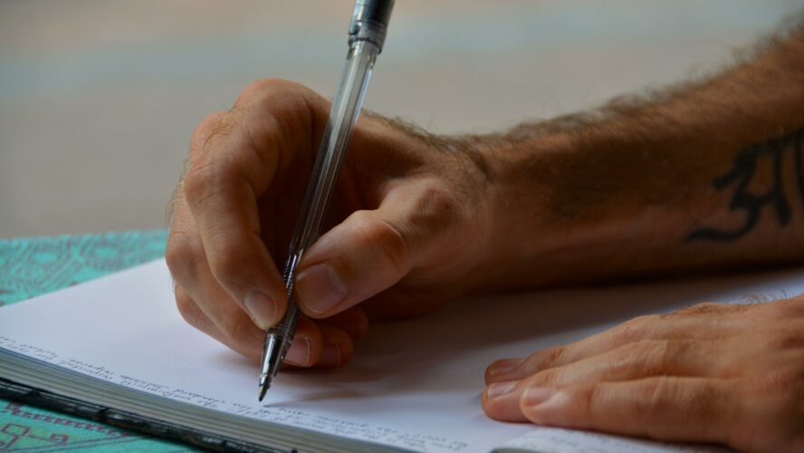 A man's hand holding a pen signing a letter.