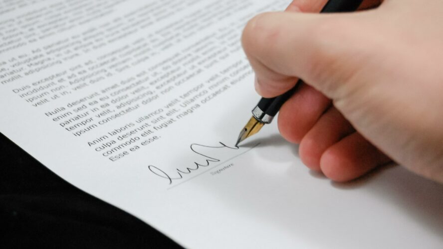 A hand holding a fountain pen signing an important document.