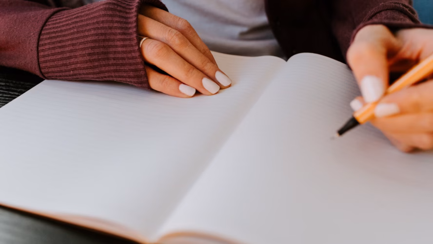 Woman holding a pen, about to start writing in her notebook.