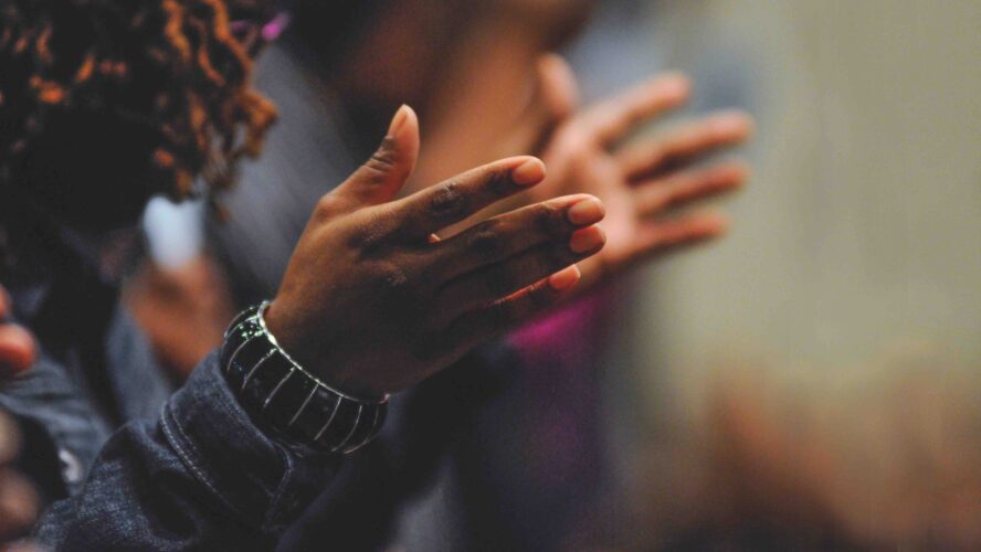 Woman holding her hands in front of her, praying with her head bowed.