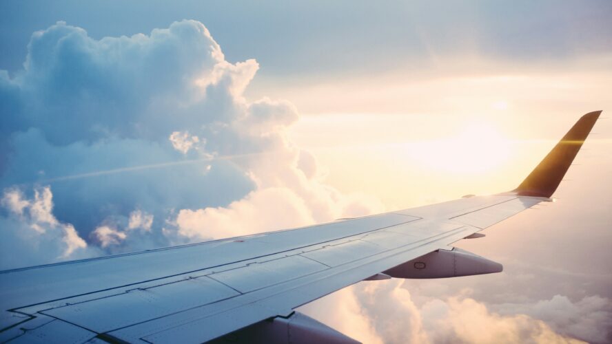 A plane in the air at high altitude showing the plane's wing. You can see the sunrise in the background.