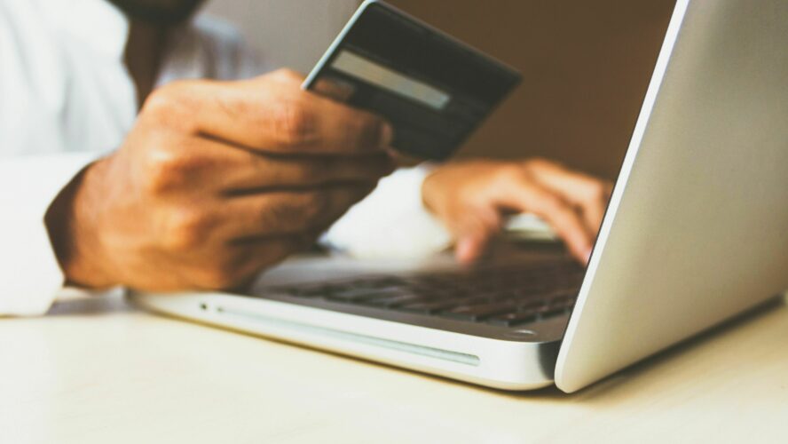 close up of someone holding up a credit card while looking at a laptop