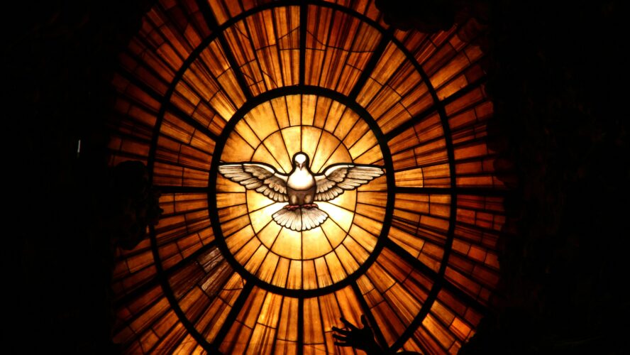 Image of a stained glass window with a dove in the middle and orange and yellow stained glass surrounding it