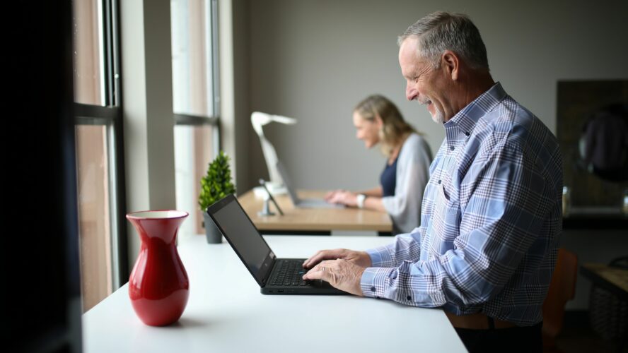 Older man happily using a laptop at a desk after finding out he's entitled to pension credit using the CAP benefits calculator.