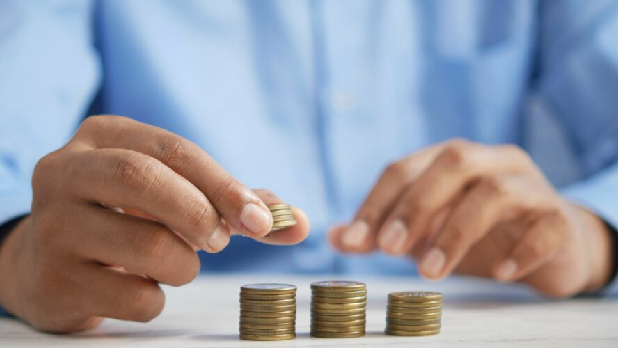 Mans hands counting coins in piles trying to budget in the cost of living crisis.