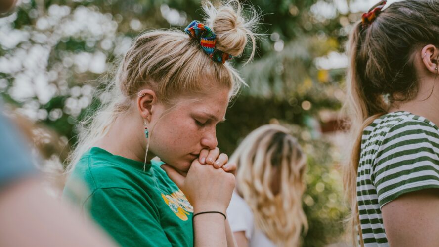 Image of a young person with their eyes closed and facing their head towards the ground, praying