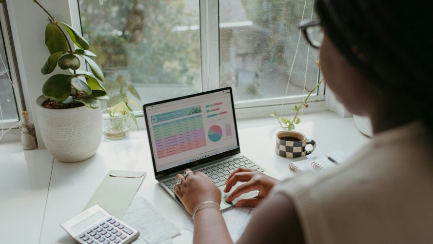 A woman sat at a desk looking at a laptop, seeing how her finances will be impacted by the Spring Budget 2024.