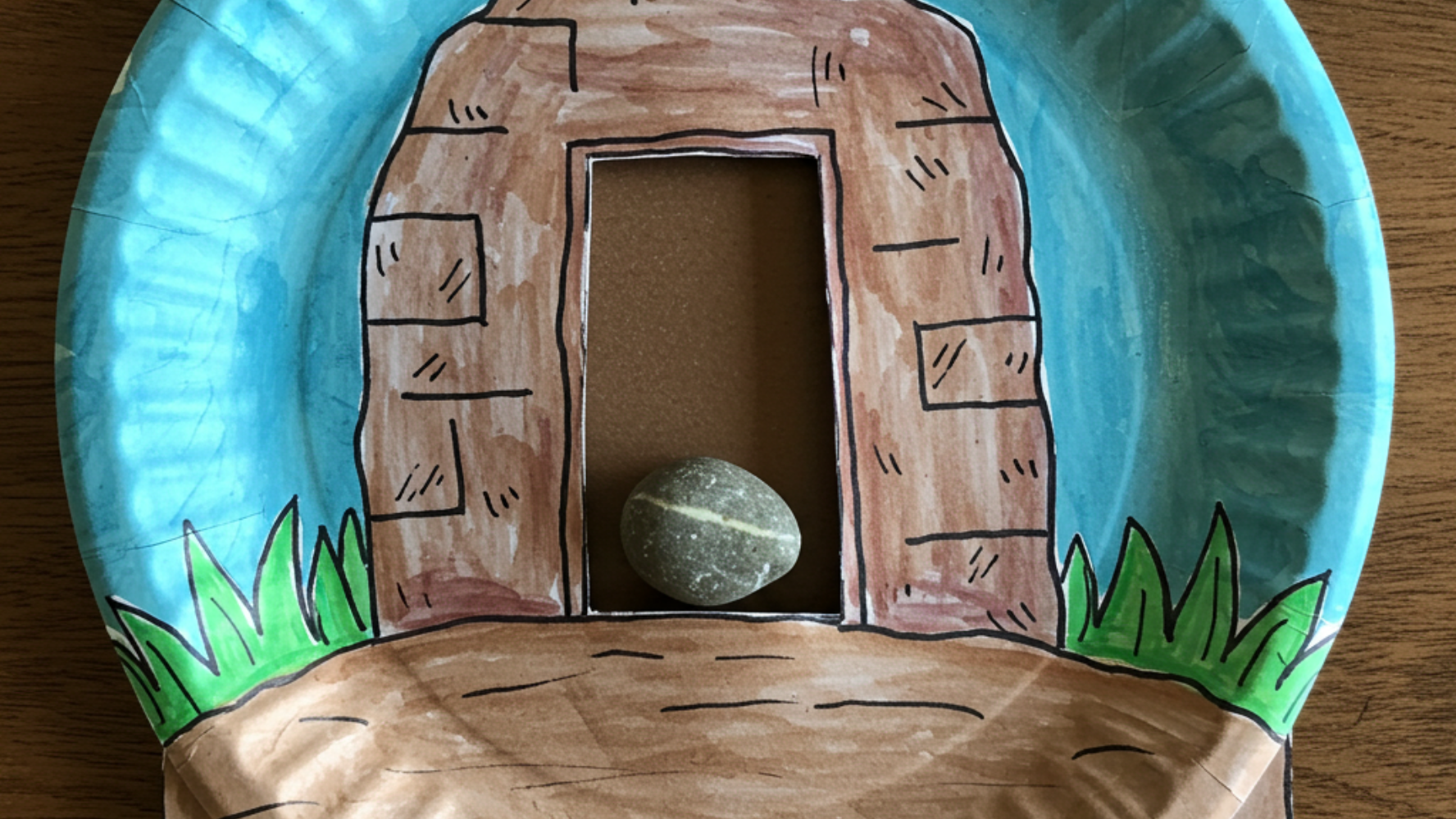 Religious Easter craft showing a paper plate with a cutout in the middle, looking like a tomb, with a rock stuck on top of the door