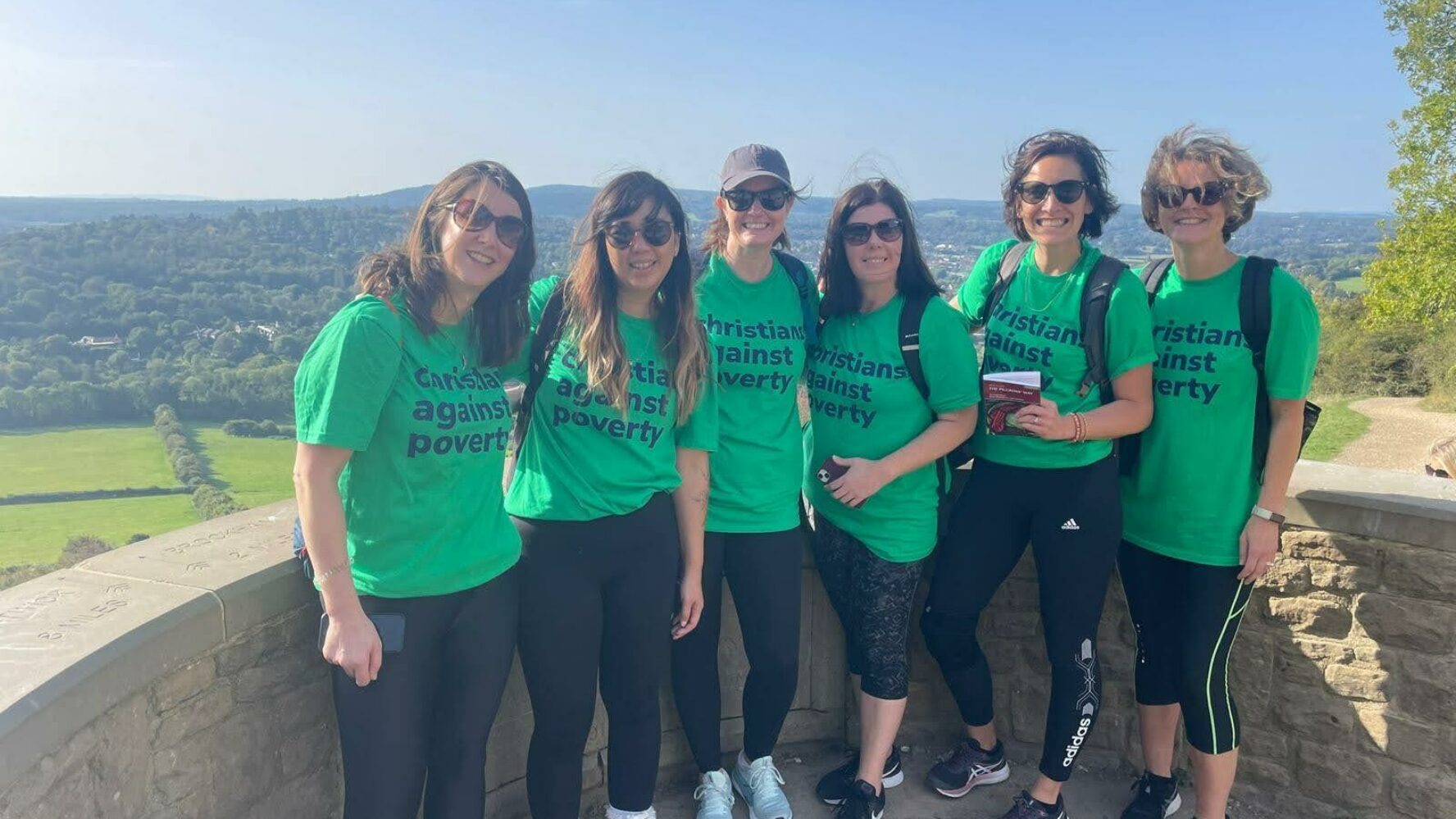 Six women stood together in green Christians Against Poverty t-shirts, wearing trainers and on a charity walk