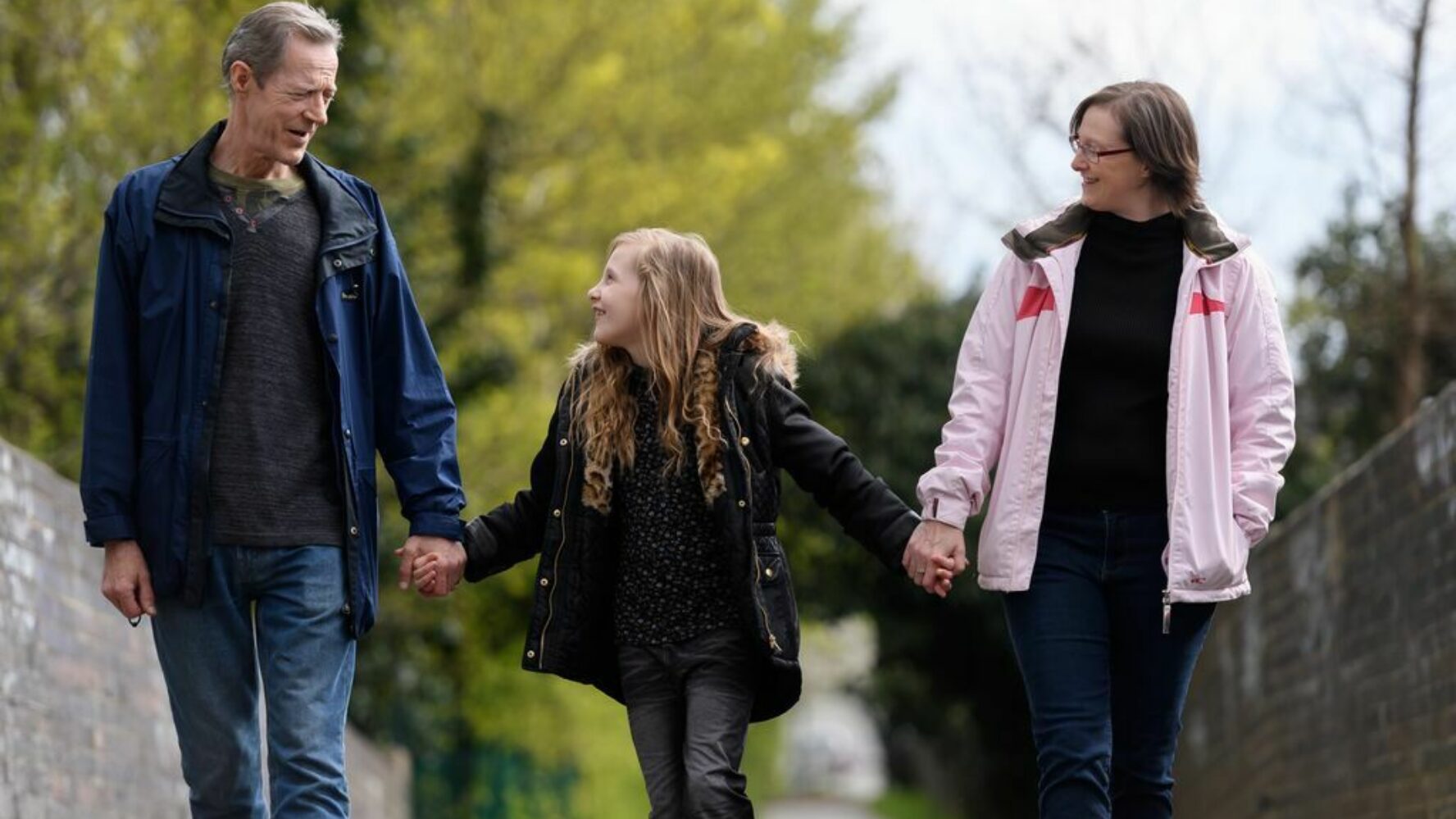 Male and female holding hands with young girl, walking and smiling at each other.