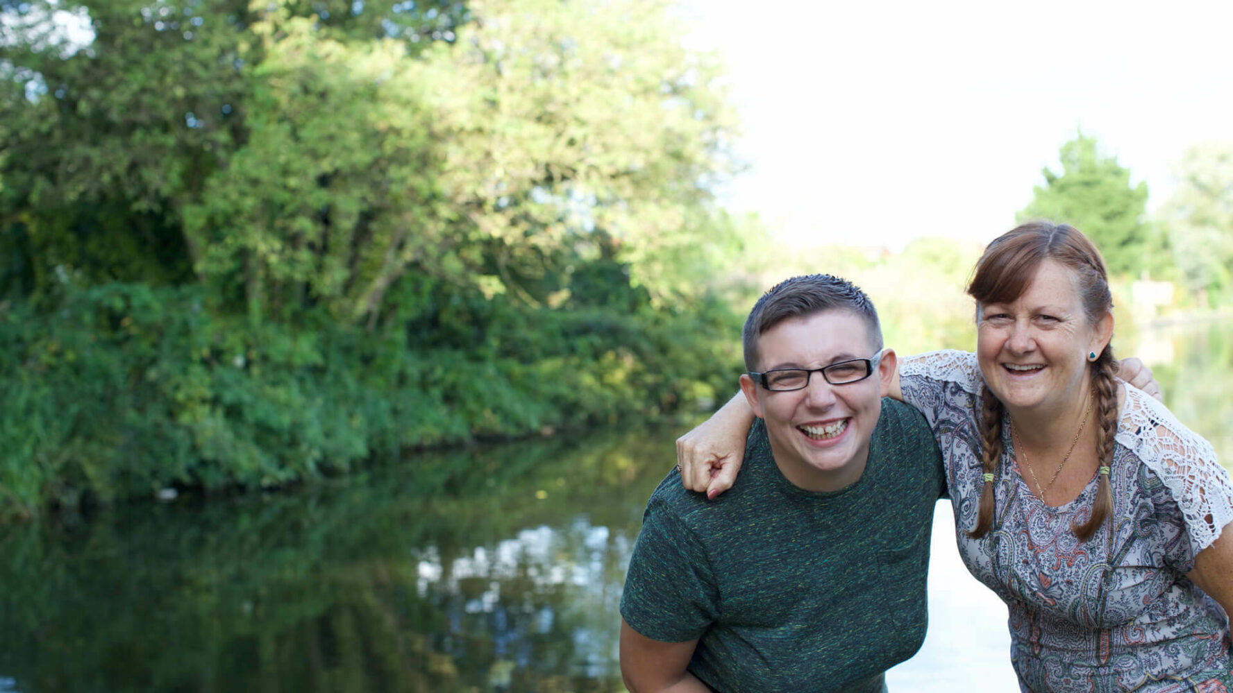 Two women smiling with their hands around each other walking alongside a canal.