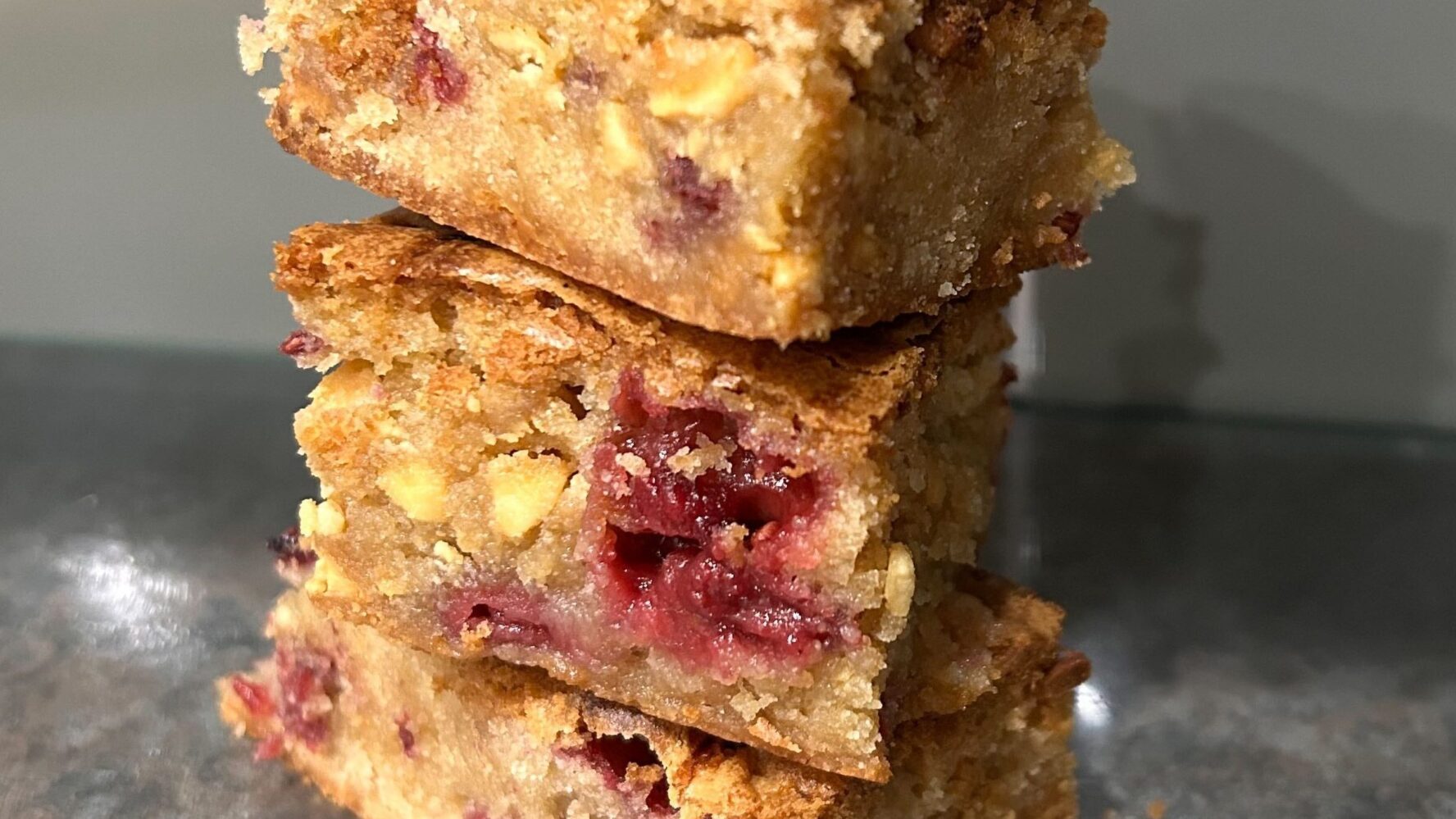 A stack of three white chocolate and raspberry blondies on a kitchen wroksurface
