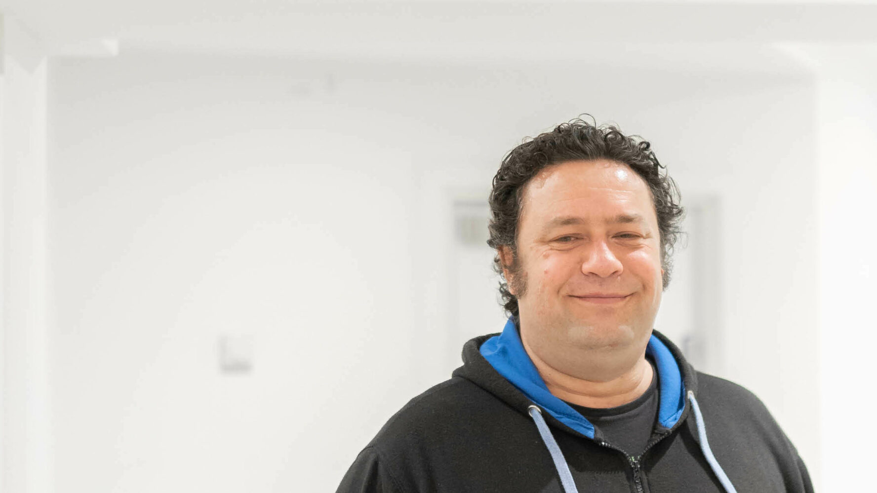 Older male stood indoors smiling at the camera.