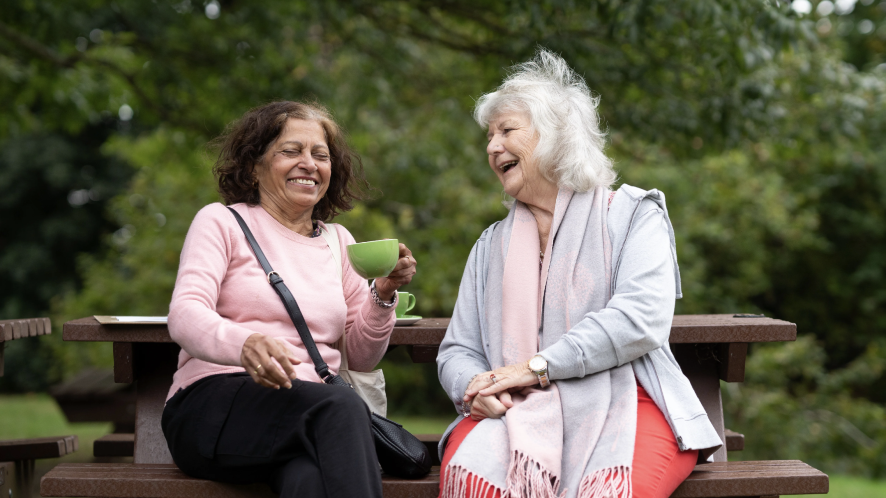 Two older women sat on a park bench laughing together