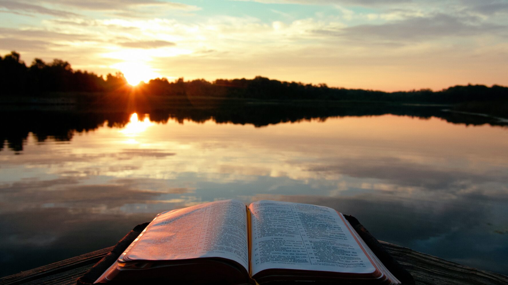Image of a sunset across a lake, with a Bible open on a bench