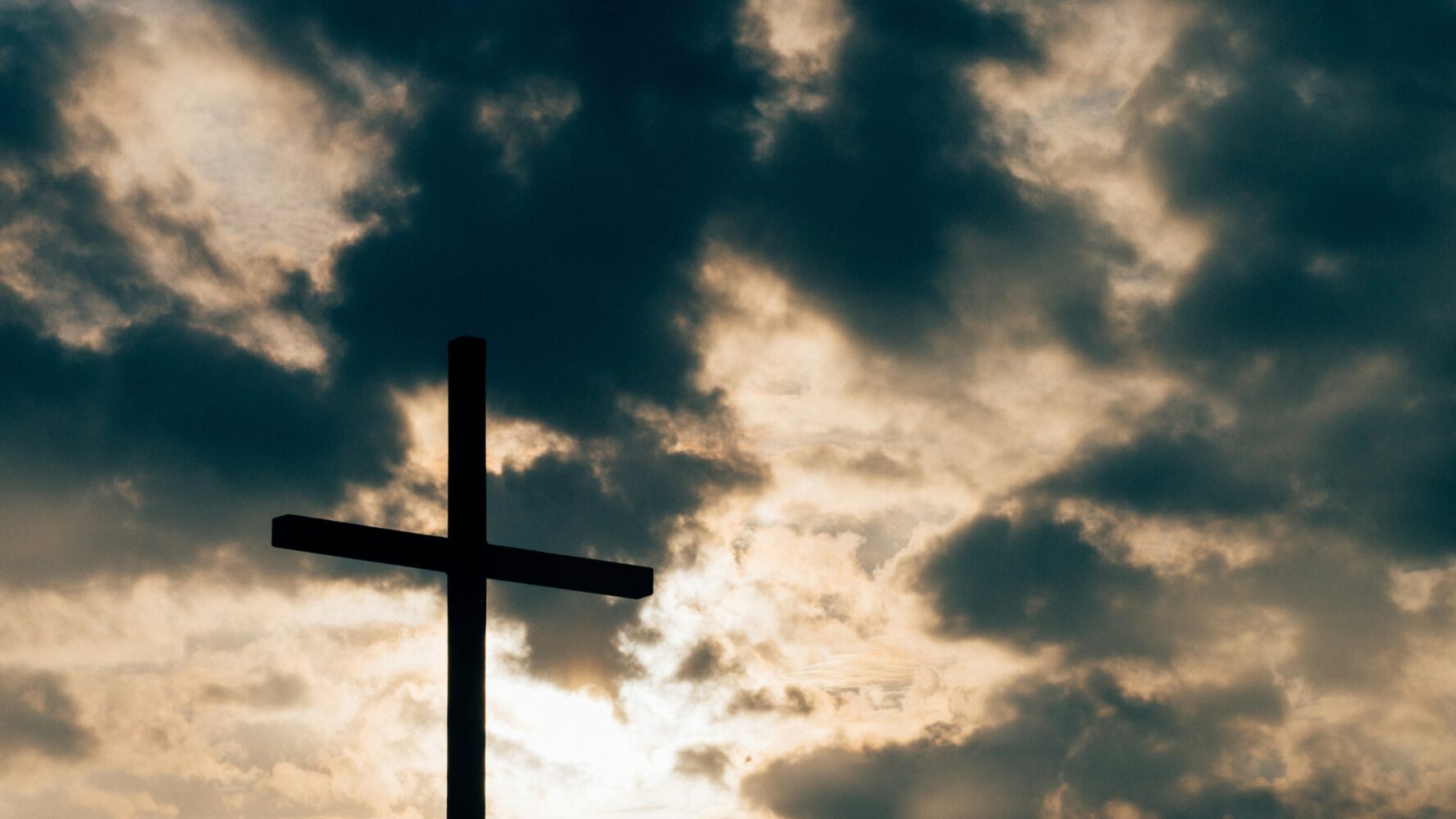 Image of a large cross - a low angle shot looking up at the sun behind the clouds with the cross in the foreground
