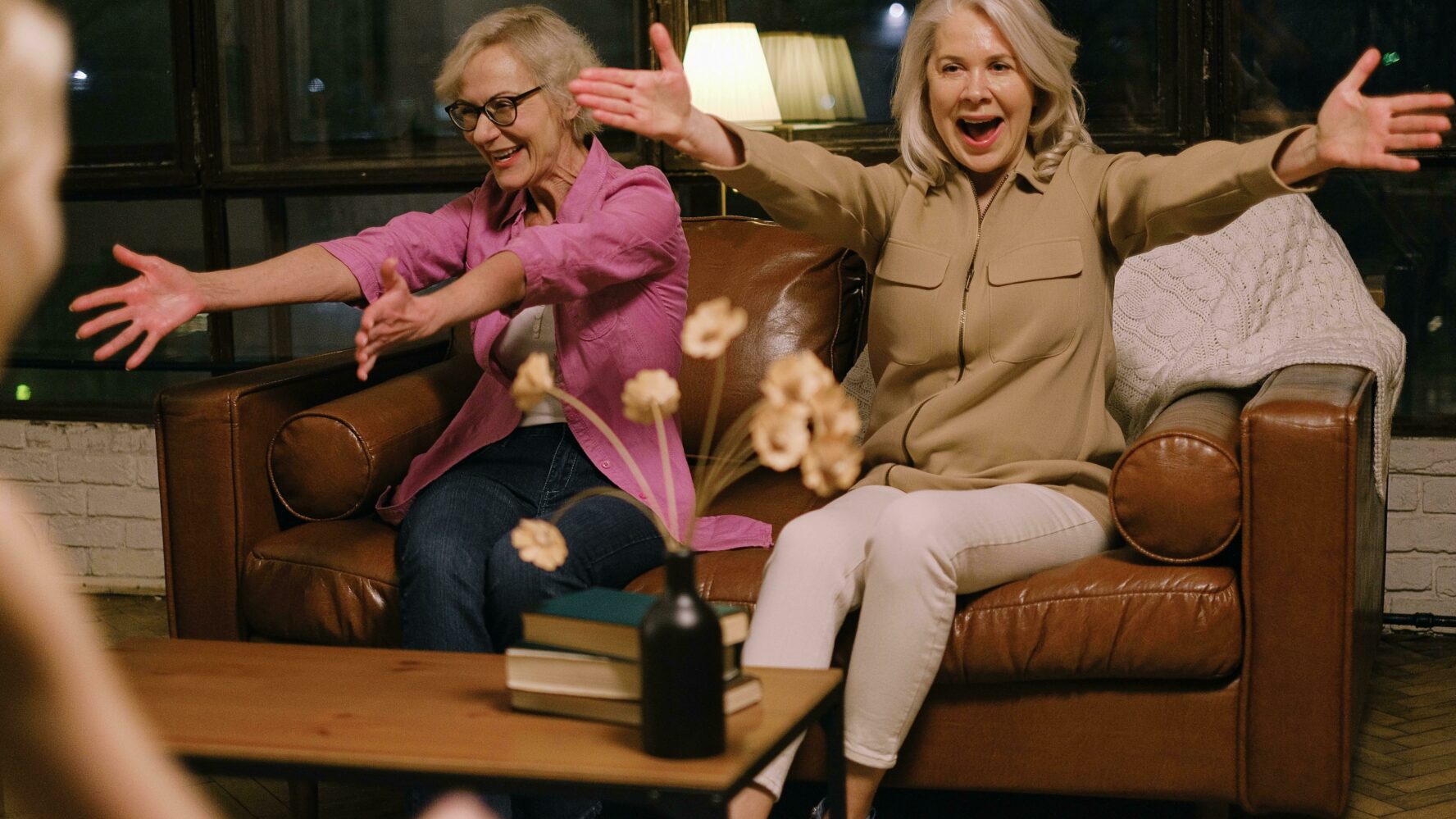 Two grandmothers sitting on a brown sofa with their arms open wide