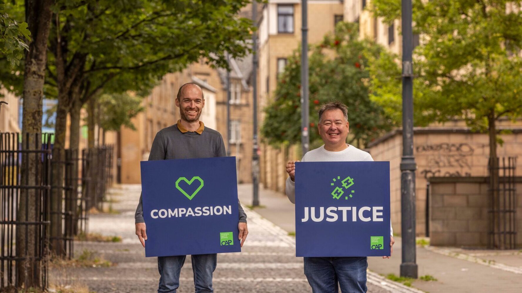 Two CAP employees, Duncan and Gordan, holding signs that read 'compassion' and 'justice'