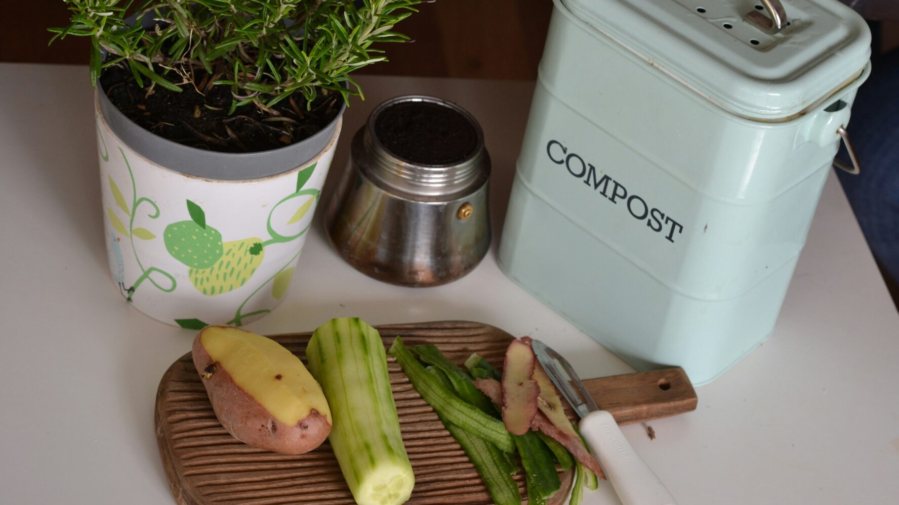 A kitchen counter with chopped up vegetables next to a ceramic compost tin.