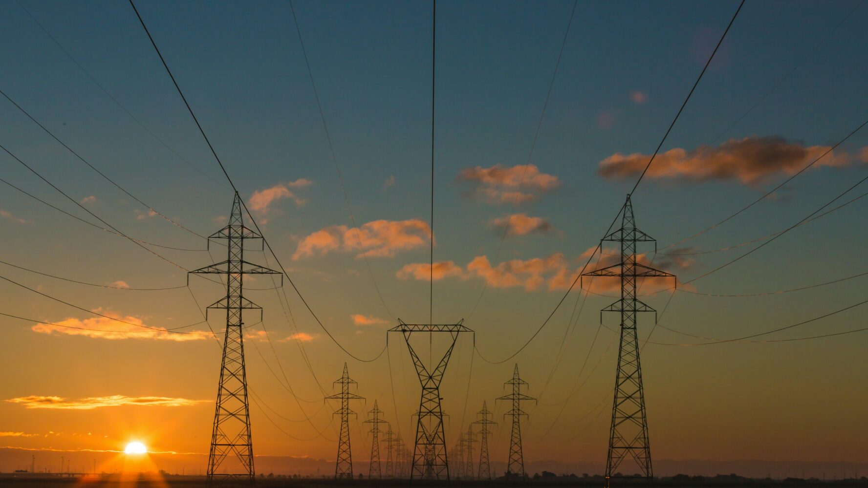 An image showing a sunset over a field with pylons.