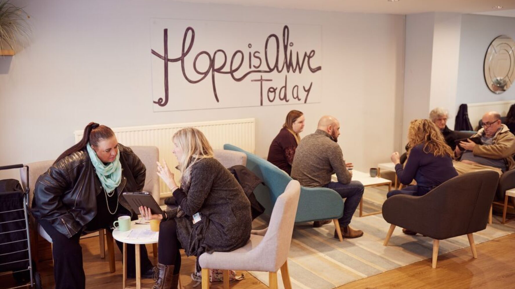 Image of a church community group with people sat around tables talking. The wall quote reads 'hope is alive today'