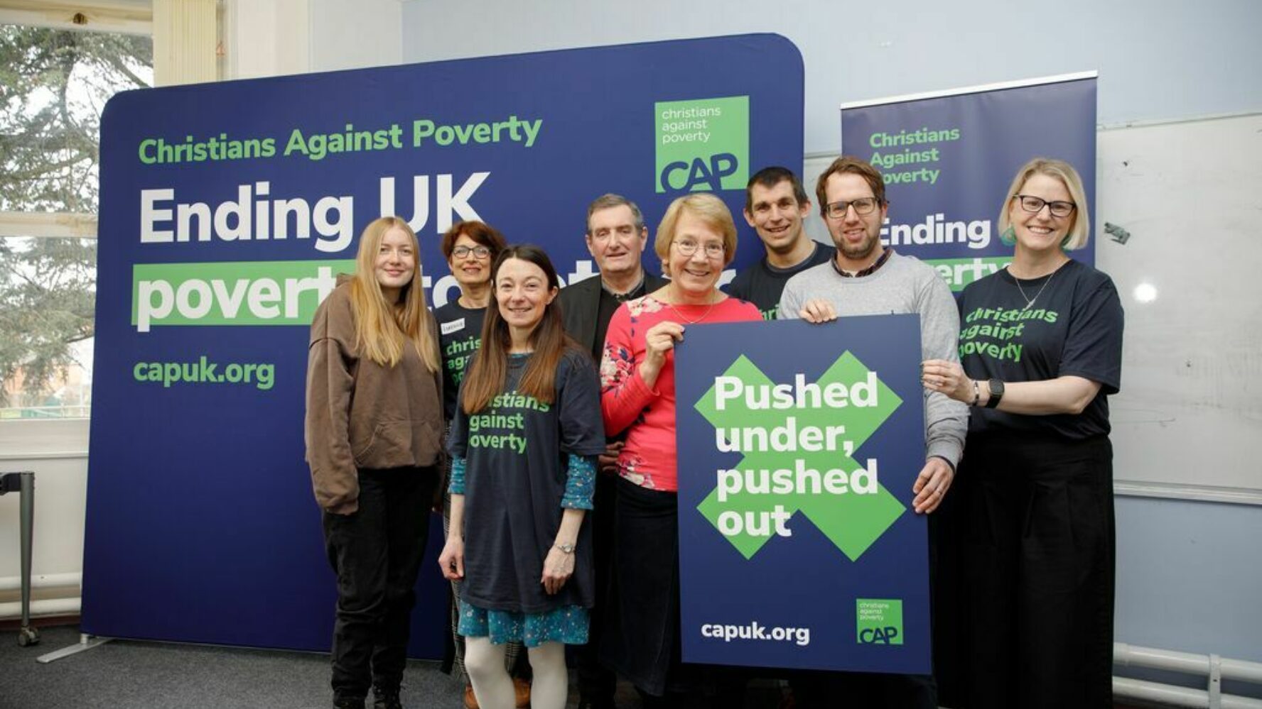 CAP campaigners stood together at a media event, holding up a promotional sign reading 'Pusher under, pushed out' - A 2024 CAP report