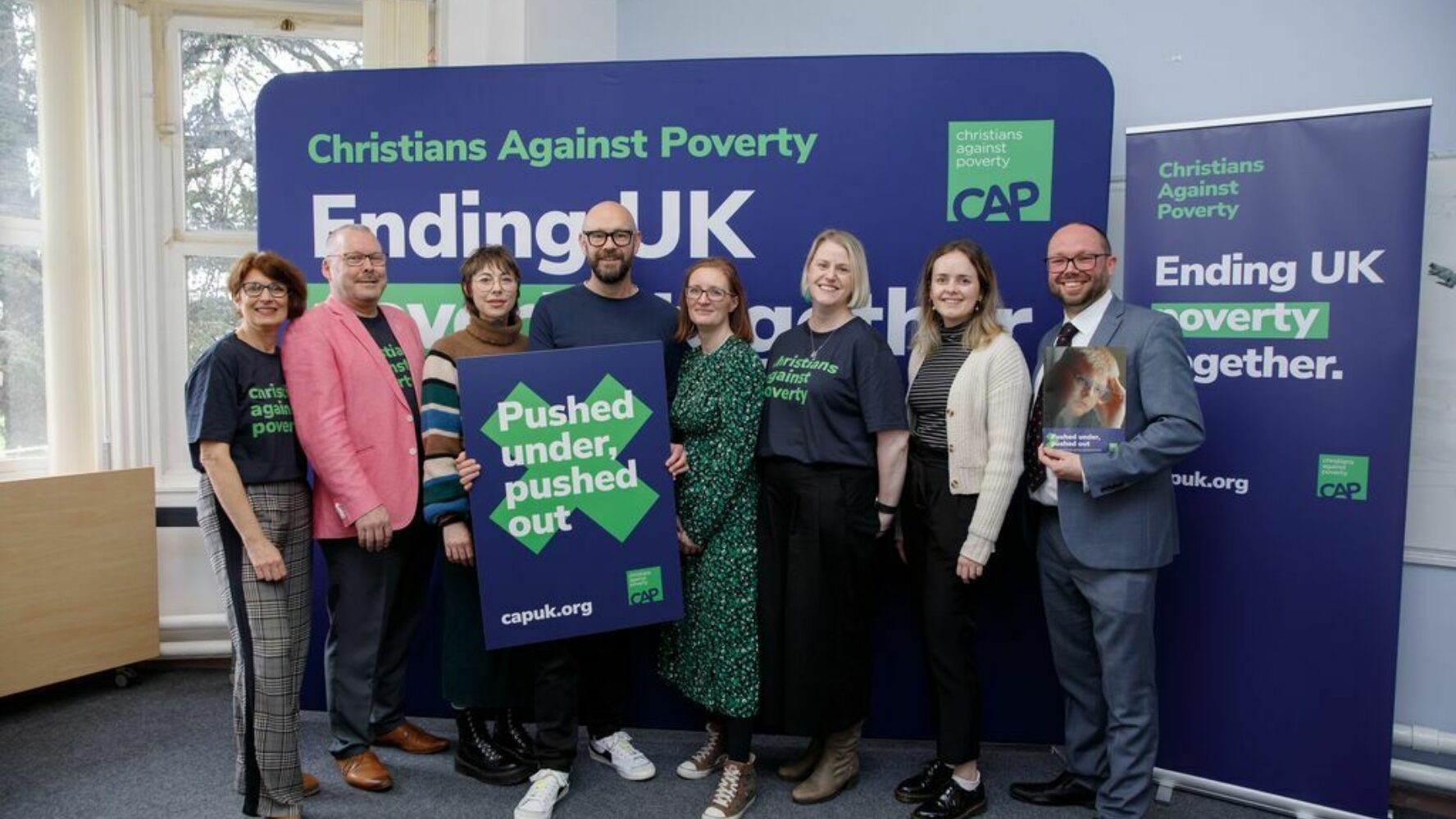 CAP frontline and head office staff promoting the new report, pushed under pushed out, stood together holding a promotional sign.