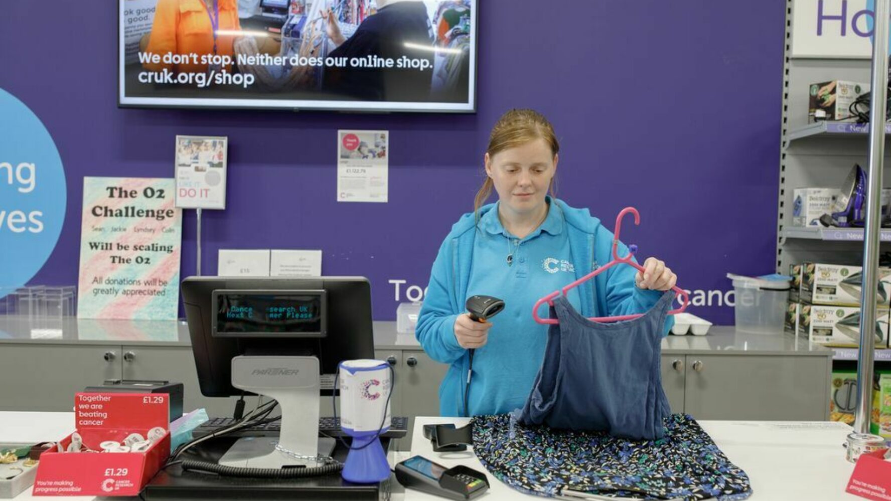 CAP client, Lyndsey, volunteering at her local charity shop, scanning items of clothing at the till