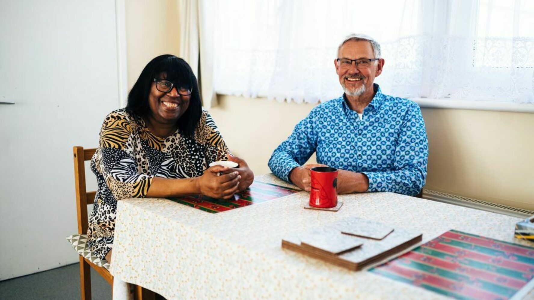 CAP client sat with Debt Coach at a table, drinking a cup of tea and smiling