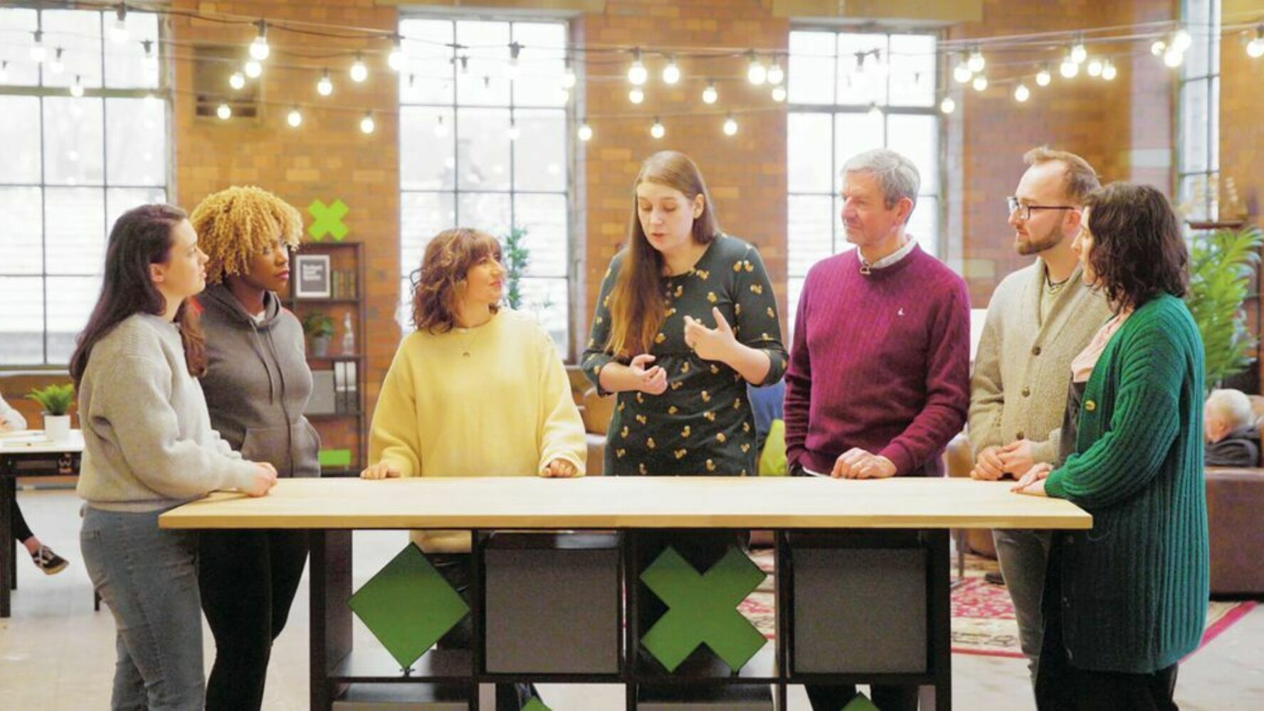 Seven people stood around a long table talking during a CAP money coaching workshop