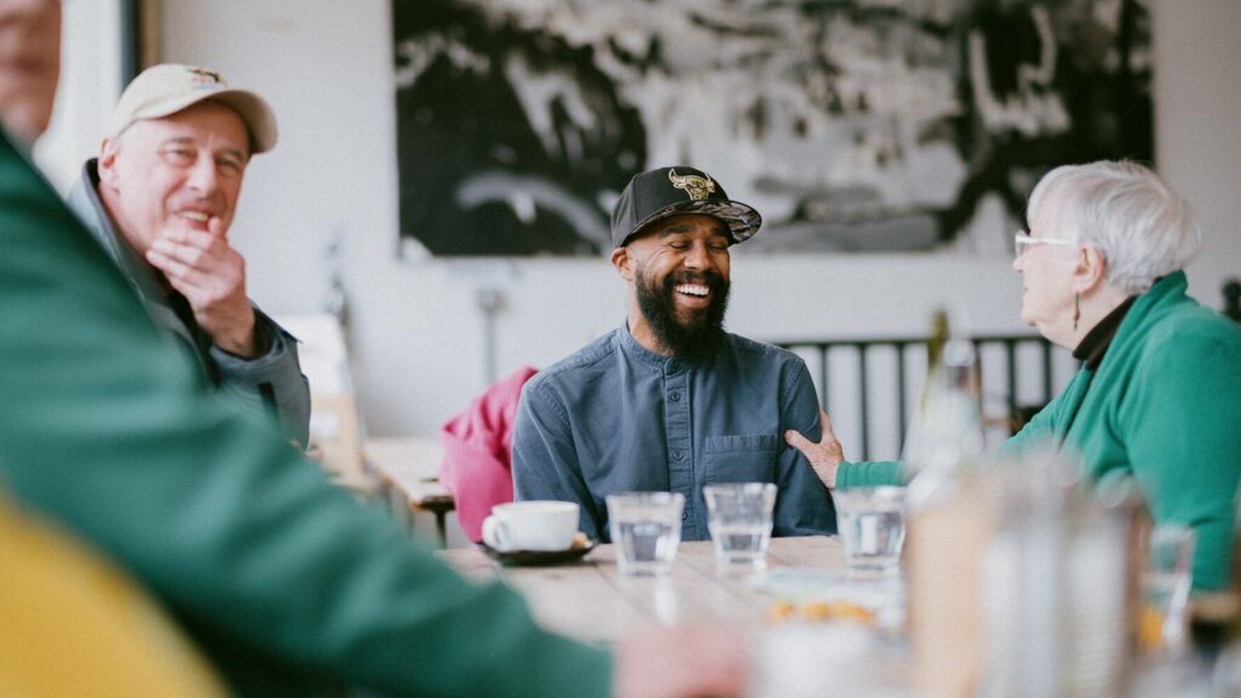 Image of a church leader sat around a table in a cafe with people from his local community, laughing