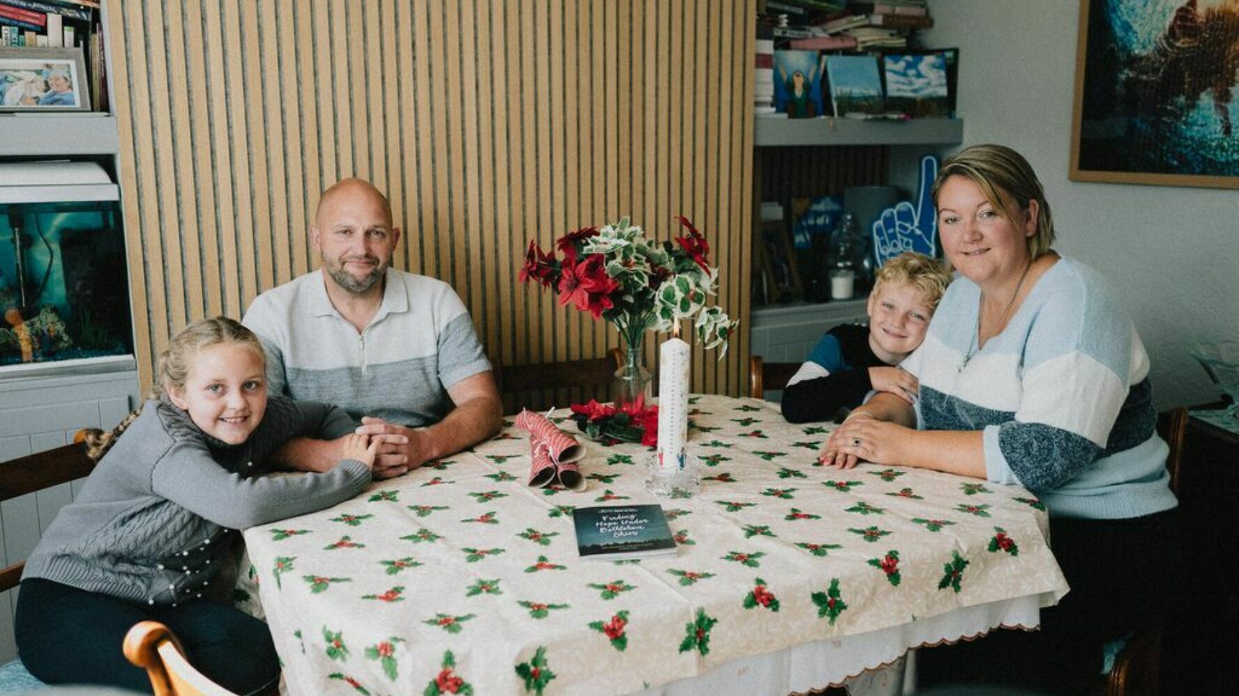 Image of a family of four - two adults and two children - sat around a Christmas table smiling at the camera