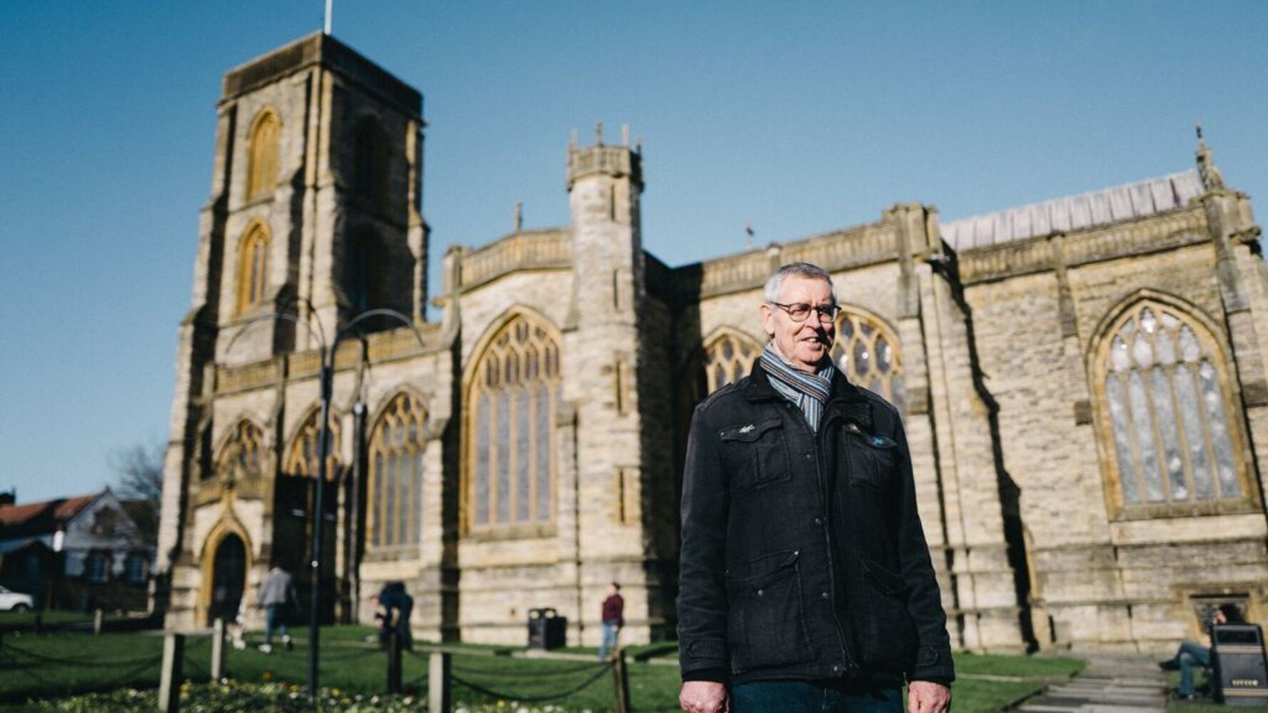 Picture of retired debt centre manager, similing, stood outside cathedral.
