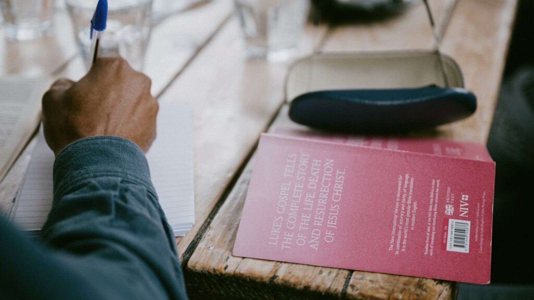 A person writing on a notepad, with the gospel of Luke open next to him.