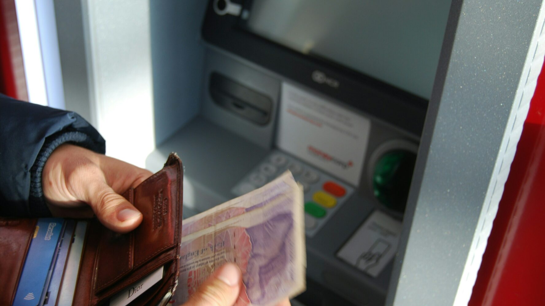 Someone getting money out of a cash point and putting it in their wallet