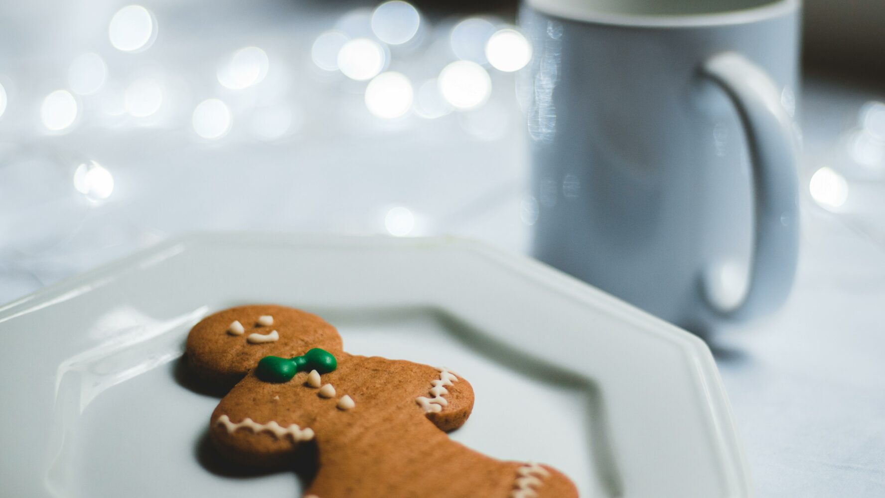 A festive gingerbread man on a plate next to a mug.