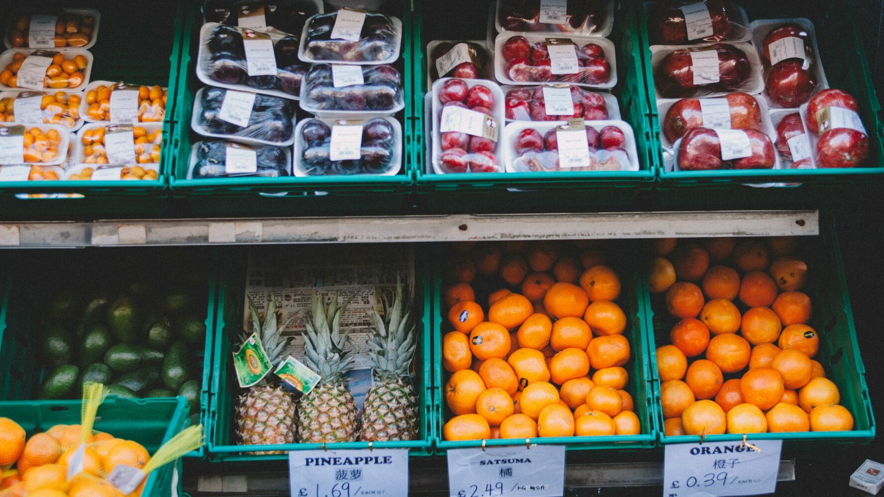 Green crates in a shop filled with plums, apples, pineapples and oranges