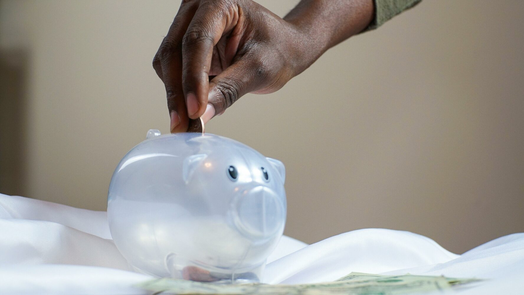 A hand putting coins into a white piggy bank.
