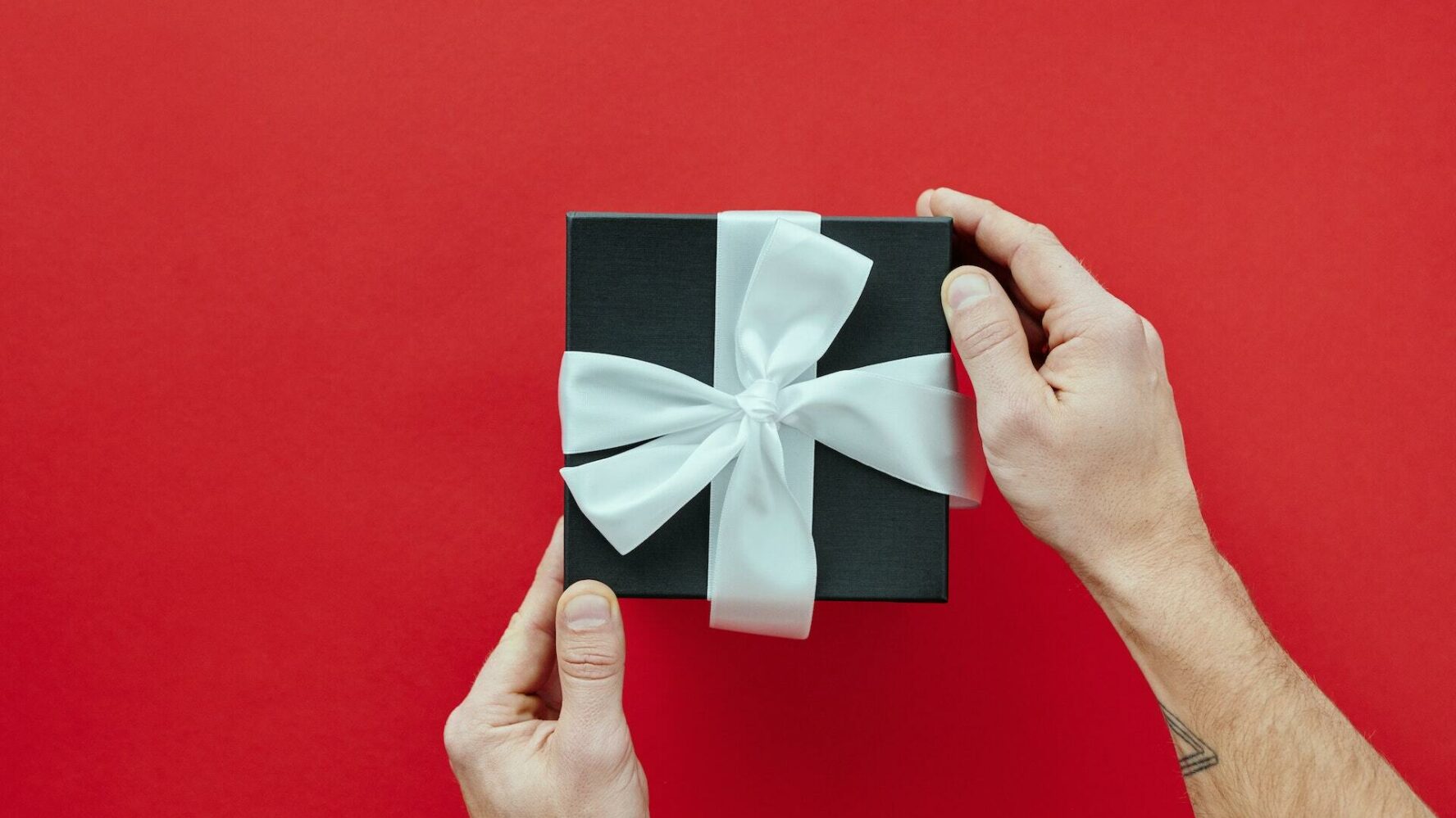 two hands hold a gift in a black box topped with a bow