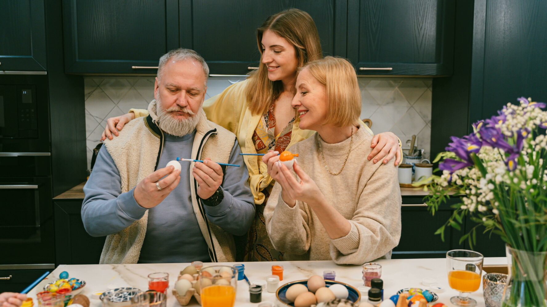 Image of a couple with their young adult daughter, painting eggs together