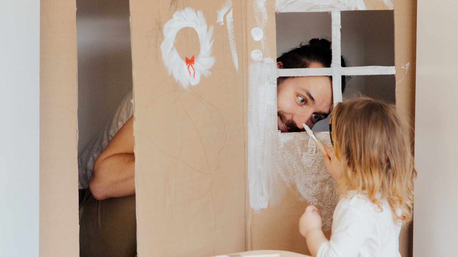 A dad playing in a cardboard house with their child.