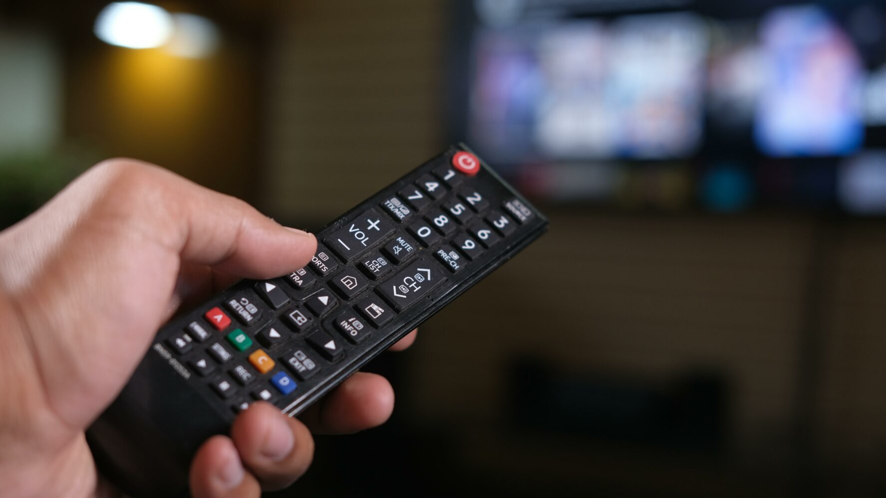 A hand holding a remote control changing channels on a tv