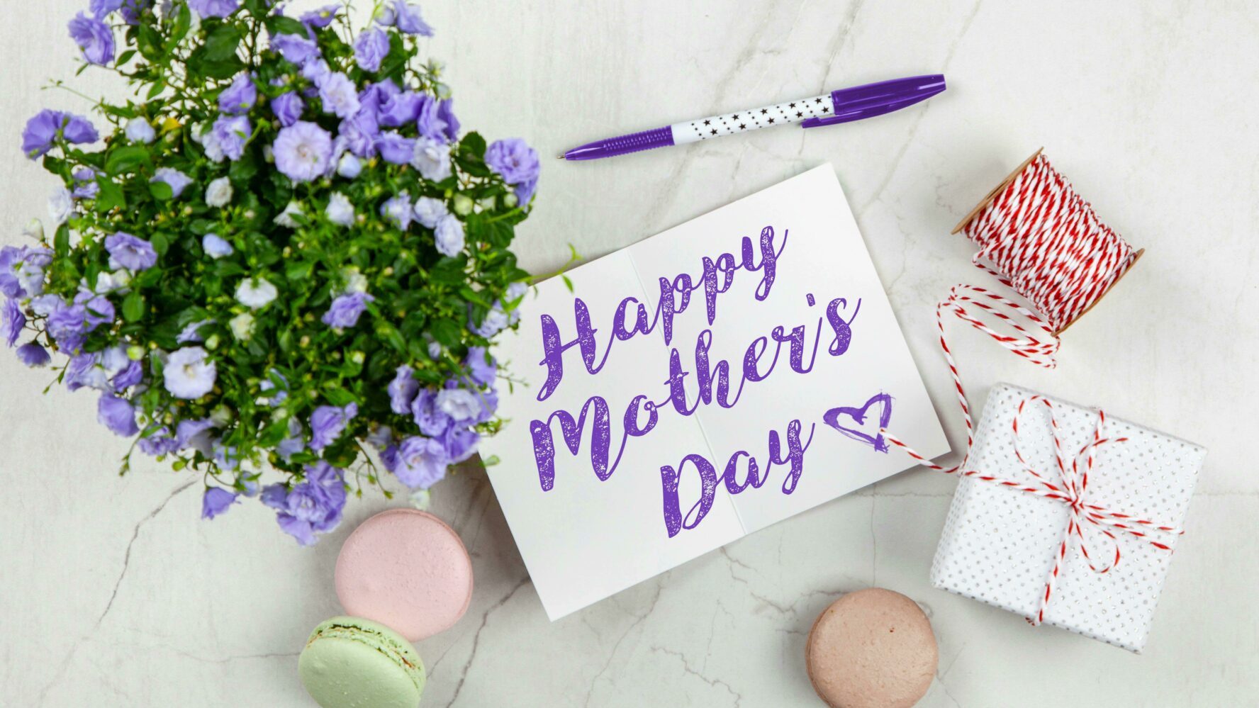 A Mother's day card, purple flowers, small gift and macarons.