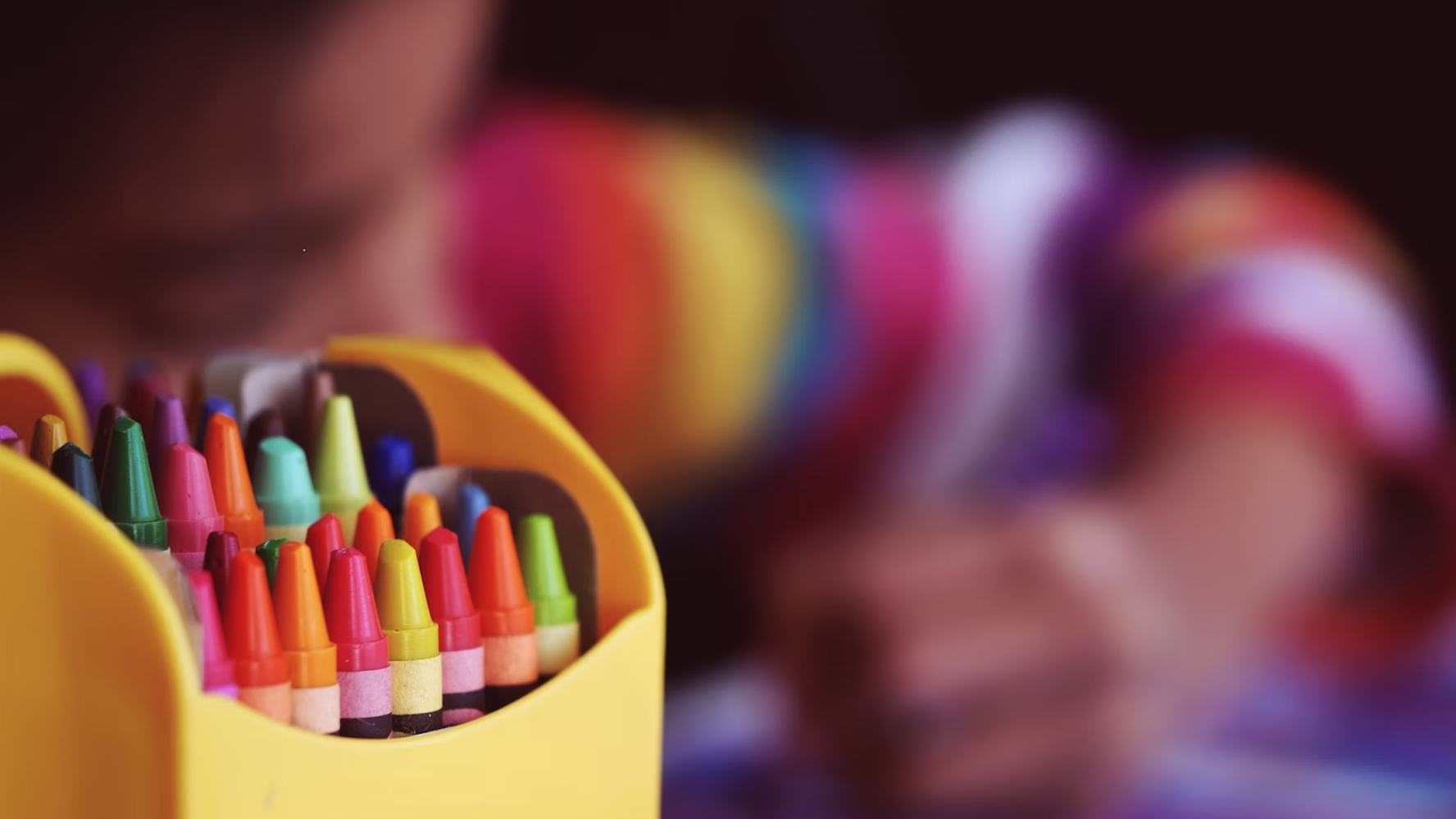 Image of some pencil crayons with a blurred background of a child drawing