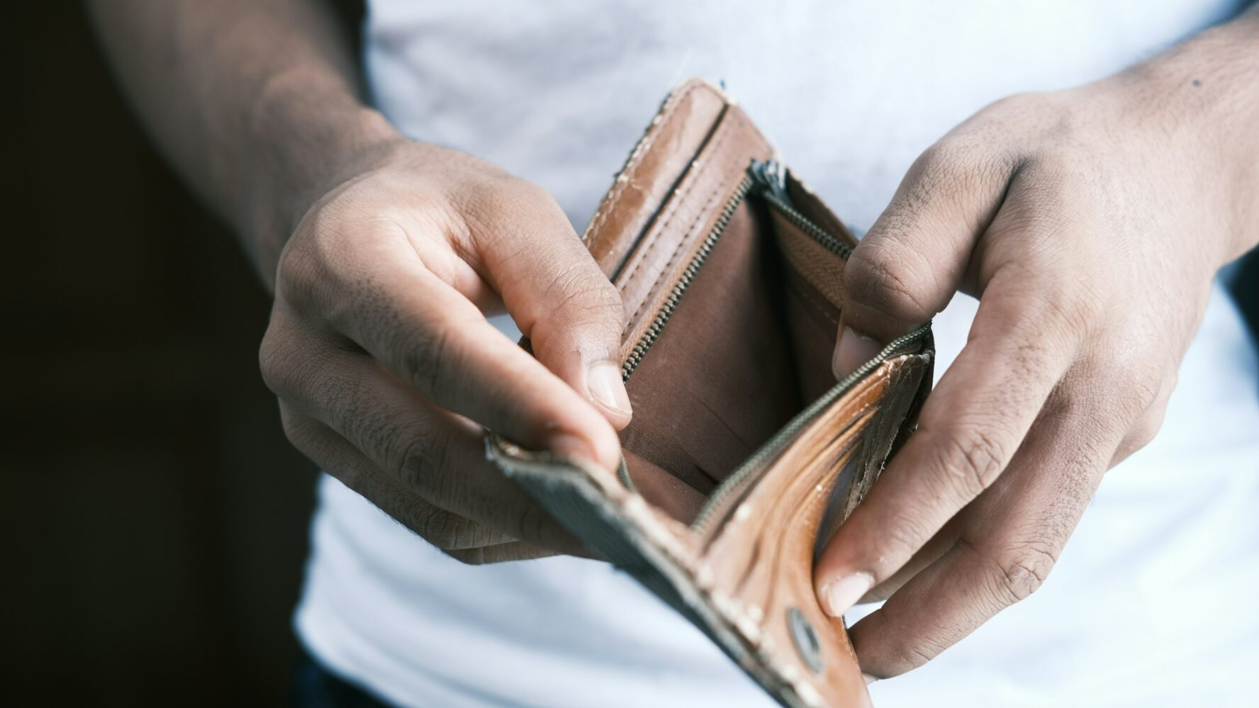 Photo showing a person's hands, opening a brown, empty wallet