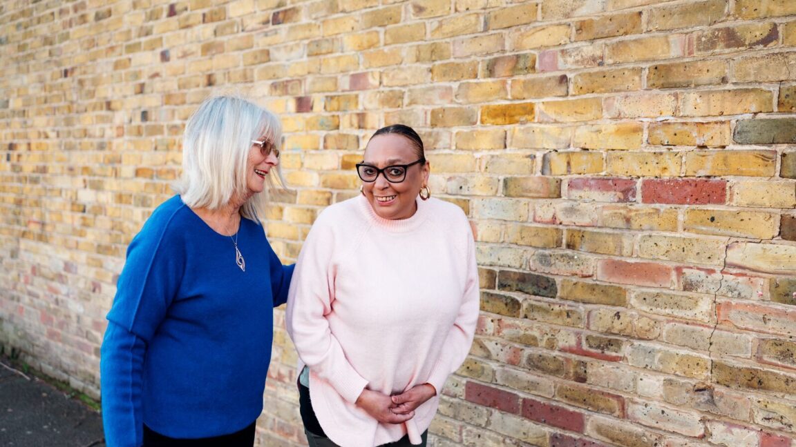 CAP client, Sharon, outside walking with a debt coach's arm around her, smiling at the camera